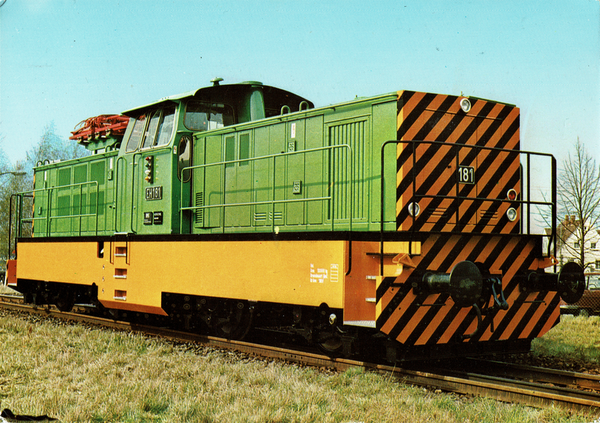 Eine grüne Lokomotive mit Stomabnehmer im Hintergrund steht auf einem Gleis. Die Fronteiete ist gelb-schwarz gestrichen. Der Unterbau verkleidet und mit Gelb lackiert.
