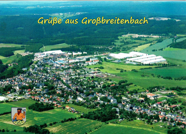 Man kann eine Luftbilduafnahme von Großbreitenbach sehen. Viel grün, viele Häuser.  Am oberen rechten Ende eine große Industriehallenanlage. Der Hintergrund geht etwas in Blaue aus